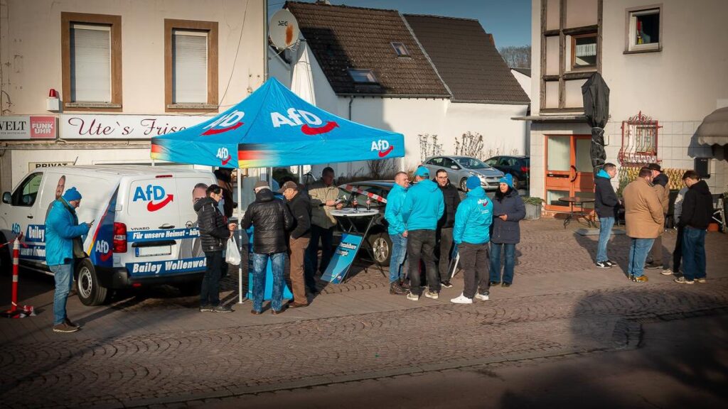 AfD-Infostand mit blauem Pavillon auf einem Platz in Selters. Mehrere Bürgerinnen und Bürger stehen im Gespräch mit Mitgliedern, Informationsmaterial wird ausgegeben.