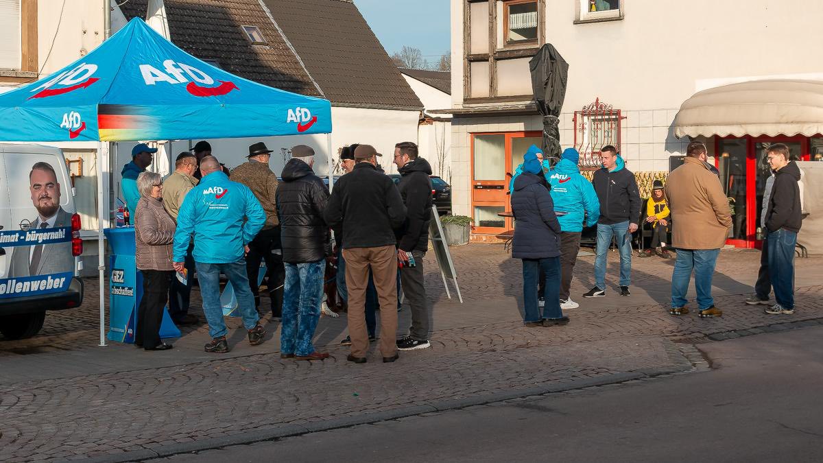 AfD-Infostand mit blauem Pavillon auf einem Platz in Selters. Mehrere Personen führen Gespräche, ein Informationsfahrzeug steht daneben, Passanten bleiben stehen.